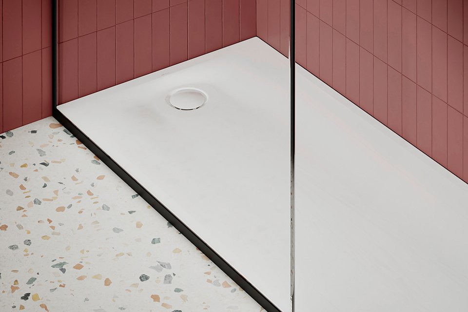 Bac à douche blanc extra-plat de marque BETTE dans une salle de bain moderne avec murs carrelés rouge foncé et sol en terrazzo.